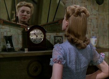 Movie still from “This Happy Breed” (1944), directed by David Lean – A woman looking in a mirror with a clock in front of her face; Close Up shot, Over the shoulder angle