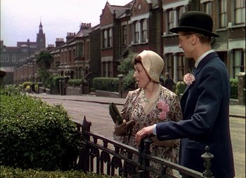Movie still from “This Happy Breed” (1944), directed by David Lean – A man and a woman standing next to each other on a sidewalk; Wide shot, Over the shoulder angle