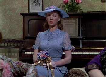 Movie still from “This Happy Breed” (1944), directed by David Lean – A woman holding a bouquet of flowers while standing in front of a piano; Medium shot, Over the shoulder angle