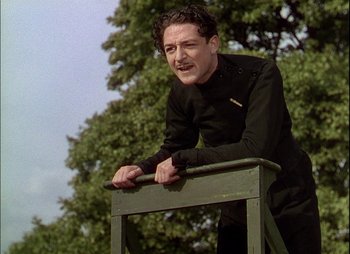 Movie still from “This Happy Breed” (1944), directed by David Lean – A man leaning on a bench near a tree; Medium shot, Low angle