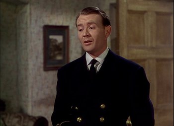 Movie still from “This Happy Breed” (1944), directed by David Lean – A man in a suit and tie standing in front of a wall; Medium shot, High angle