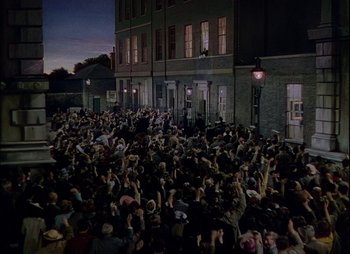 Movie still from “This Happy Breed” (1944), directed by David Lean – A crowd of people gathered in front of a building at night; Extreme Wide shot, High angle