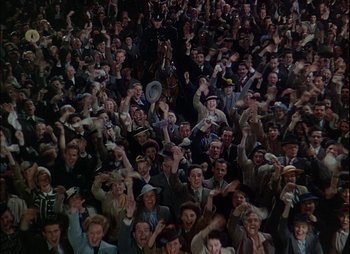 Movie still from “This Happy Breed” (1944), directed by David Lean – A large group of men in suits and hats raising their hands in the air; Extreme Wide shot, High angle