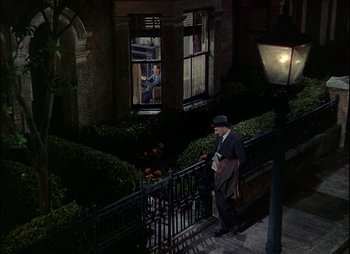 Movie still from “This Happy Breed” (1944), directed by David Lean – An old man in a suit and hat is standing on the steps of a building; Wide shot, High angle