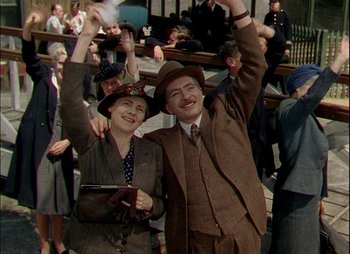 Movie still from “This Happy Breed” (1944), directed by David Lean – A man and a woman are standing in front of a group of people; Medium shot, Low angle