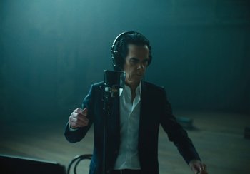 Movie still from “This Much I Know to Be True” (2022), directed by Andrew Dominik – A man wearing headphones and a microphone in front of a microphone; Medium shot, Low angle