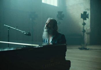 Movie still from “This Much I Know to Be True” (2022), directed by Andrew Dominik – A man with a long beard sitting at a piano; Medium shot, Over the shoulder angle
