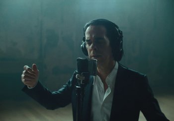 Movie still from “This Much I Know to Be True” (2022), directed by Andrew Dominik – A man in a black suit is singing into a microphone; Medium shot, Over the shoulder angle