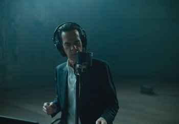 Movie still from “This Much I Know to Be True” (2022), directed by Andrew Dominik – A man wearing headphones and a microphone in front of a microphone; Medium shot, Low angle