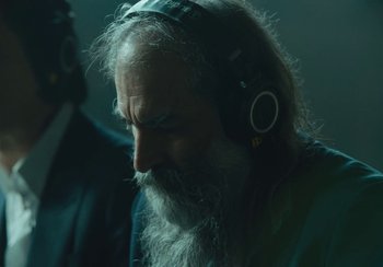 Movie still from “This Much I Know to Be True” (2022), directed by Andrew Dominik – An old man with long white beard wearing headphones; Close Up shot, Over the shoulder angle
