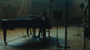 Movie still from “This Much I Know to Be True” (2022), directed by Andrew Dominik – A man sitting at a piano in a dark room; Wide shot, High angle