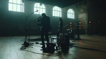 Movie still from “This Much I Know to Be True” (2022), directed by Andrew Dominik – A group of people playing instruments in a room; Wide shot, Low angle