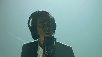 Movie still from “This Much I Know to Be True” (2022), directed by Andrew Dominik – A man wearing headphones and a microphone in front of a microphone; Close Up shot, Low angle