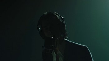 Movie still from “This Much I Know to Be True” (2022), directed by Andrew Dominik – A person with a microphone in a dark room; Medium shot, Low angle