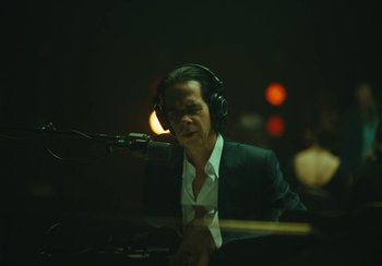 Movie still from “This Much I Know to Be True” (2022), directed by Andrew Dominik – A man wearing headphones sitting at a piano; Medium shot, Low angle