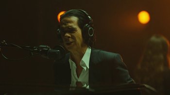 Movie still from “This Much I Know to Be True” (2022), directed by Andrew Dominik – A man wearing headphones and a microphone in front of a microphone; Close Up shot, Low angle