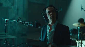 Movie still from “This Much I Know to Be True” (2022), directed by Andrew Dominik – A man wearing headphones and sitting in front of a microphone; Medium shot, Low angle