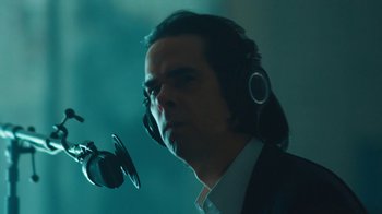 Movie still from “This Much I Know to Be True” (2022), directed by Andrew Dominik – A man wearing headphones and a suit is talking into a microphone; Close Up shot, Low angle