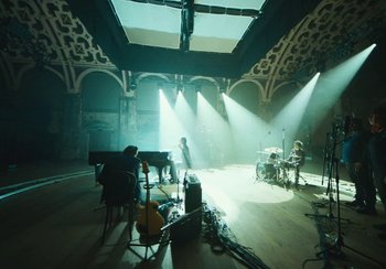 Movie still from “This Much I Know to Be True” (2022), directed by Andrew Dominik – A group of people playing musical instruments on a stage; Extreme Wide shot, High angle