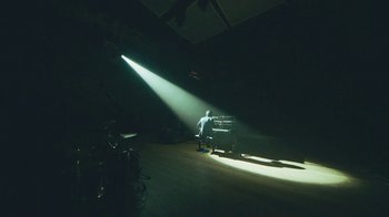 Movie still from “This Much I Know to Be True” (2022), directed by Andrew Dominik – A man standing in front of a piano in a dark room; Extreme Wide shot, High angle
