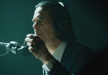 Movie still from “This Much I Know to Be True” (2022), directed by Andrew Dominik – A man in a black suit is holding a microphone; Close Up shot, Low angle