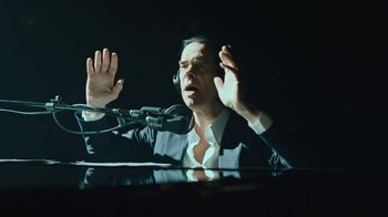 Movie still from “This Much I Know to Be True” (2022), directed by Andrew Dominik – A man in a suit and tie sitting in front of a microphone; Close Up shot, High angle