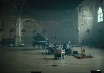 Movie still from “This Much I Know to Be True” (2022), directed by Andrew Dominik – A man sitting in front of a grand piano in an empty room; Extreme Wide shot, High angle