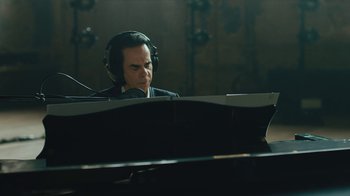 Movie still from “This Much I Know to Be True” (2022), directed by Andrew Dominik – A man wearing headphones sitting at a piano; Close Up shot, Over the shoulder angle