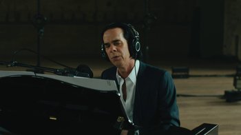 Movie still from “This Much I Know to Be True” (2022), directed by Andrew Dominik – A man wearing headphones sitting in front of a piano; Close Up shot, Low angle