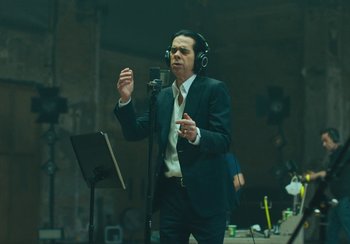 Movie still from “This Much I Know to Be True” (2022), directed by Andrew Dominik – A man in a suit and headphones is singing into a microphone; Medium shot, Low angle