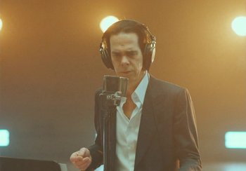 Movie still from “This Much I Know to Be True” (2022), directed by Andrew Dominik – A man wearing headphones and standing in front of a microphone; Close Up shot, Low angle