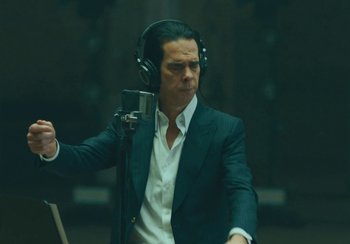 Movie still from “This Much I Know to Be True” (2022), directed by Andrew Dominik – A man in a suit is listening to a microphone; Medium shot, Low angle