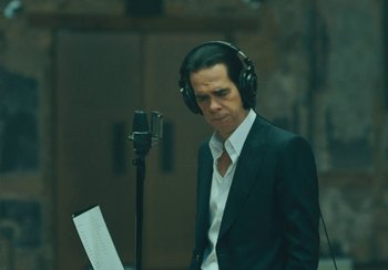 Movie still from “This Much I Know to Be True” (2022), directed by Andrew Dominik – A man wearing headphones while standing in front of a microphone; Close Up shot, Over the shoulder angle