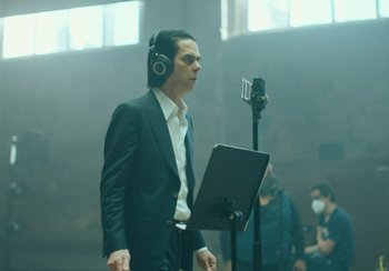 Movie still from “This Much I Know to Be True” (2022), directed by Andrew Dominik – A man wearing headphones and a microphone in front of a microphone; Medium shot, Low angle