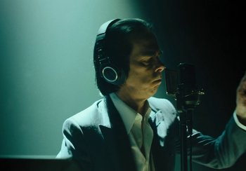 Movie still from “This Much I Know to Be True” (2022), directed by Andrew Dominik – A man wearing headphones and a suit recording; Close Up shot, Low angle