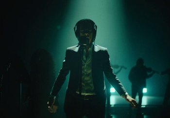 Movie still from “This Much I Know to Be True” (2022), directed by Andrew Dominik – A man in a suit and headphones in a dark room; Medium shot, Low angle