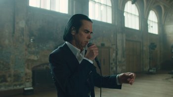 Movie still from “This Much I Know to Be True” (2022), directed by Andrew Dominik – A man in a black suit is singing into a microphone; Medium shot, Low angle