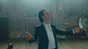 Movie still from “This Much I Know to Be True” (2022), directed by Andrew Dominik – A man in a black jacket holding a microphone; Medium shot, Low angle