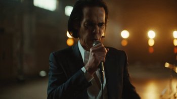 Movie still from “This Much I Know to Be True” (2022), directed by Andrew Dominik – A man in a suit and tie holding a microphone in his hand; Medium shot, Low angle