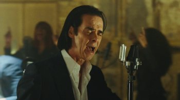 Movie still from “This Much I Know to Be True” (2022), directed by Andrew Dominik – A man in a black suit and white shirt is singing; Close Up shot, Low angle