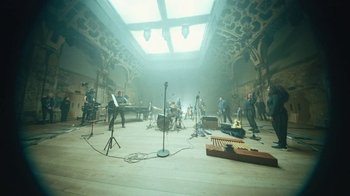 Movie still from “This Much I Know to Be True” (2022), directed by Andrew Dominik – A group of people standing in a large room; Extreme Wide shot, Low angle