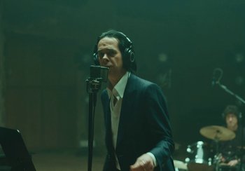 Movie still from “This Much I Know to Be True” (2022), directed by Andrew Dominik – A man in a suit and headphones is singing into a microphone; Medium shot, Low angle