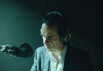 Movie still from “This Much I Know to Be True” (2022), directed by Andrew Dominik – A man wearing headphones while standing in front of a microphone; Close Up shot, Low angle