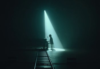 Movie still from “This Much I Know to Be True” (2022), directed by Andrew Dominik – A person standing in front of a piano on a train track; Extreme Wide shot, High angle