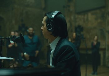 Movie still from “This Much I Know to Be True” (2022), directed by Andrew Dominik – A man with headphones on in a recording studio; Medium shot, Over the shoulder angle