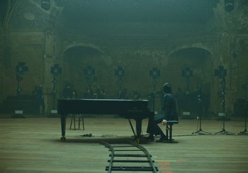 Movie still from “This Much I Know to Be True” (2022), directed by Andrew Dominik – A man sitting at a grand piano in an empty room; Extreme Wide shot, High angle