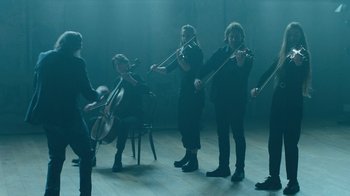 Movie still from “This Much I Know to Be True” (2022), directed by Andrew Dominik – A group of people playing musical instruments in a room; Wide shot, Low angle