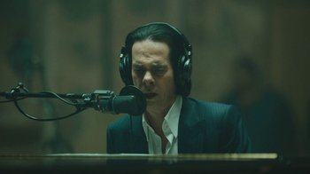 Movie still from “This Much I Know to Be True” (2022), directed by Andrew Dominik – A man in a suit and headphones is singing into a microphone; Close Up shot, Low angle