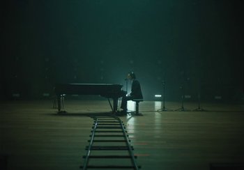 Movie still from “This Much I Know to Be True” (2022), directed by Andrew Dominik – A person sitting at a piano in a dark room; Extreme Wide shot, High angle