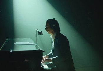 Movie still from “This Much I Know to Be True” (2022), directed by Andrew Dominik – A man playing a piano in a dark room; Medium shot, High angle